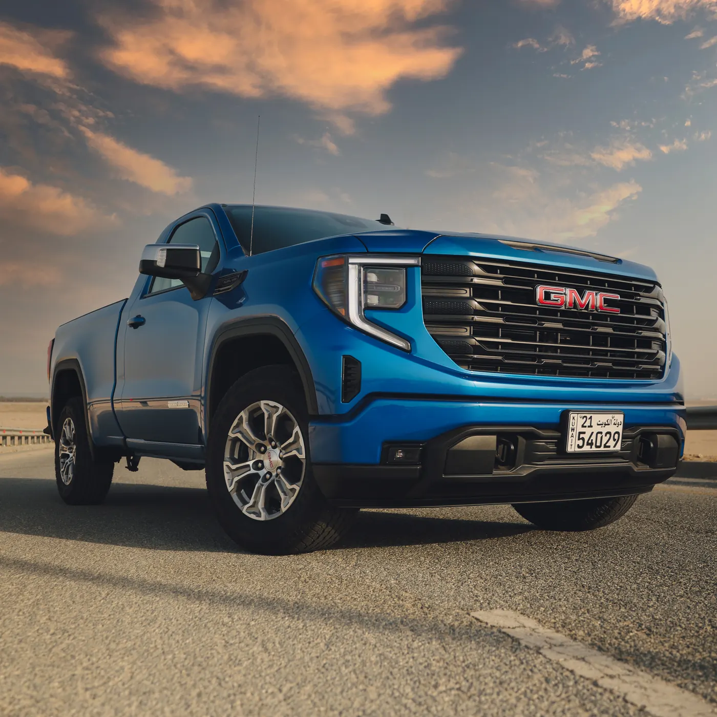 A blue GMC Sierra on an open road at golden hour